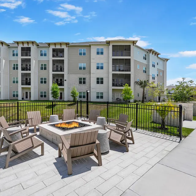 Modern Apartment Complex Outdoor Space Outdoor area of a modern apartment complex featuring a fire pit surrounded by seating, with a building in the background.