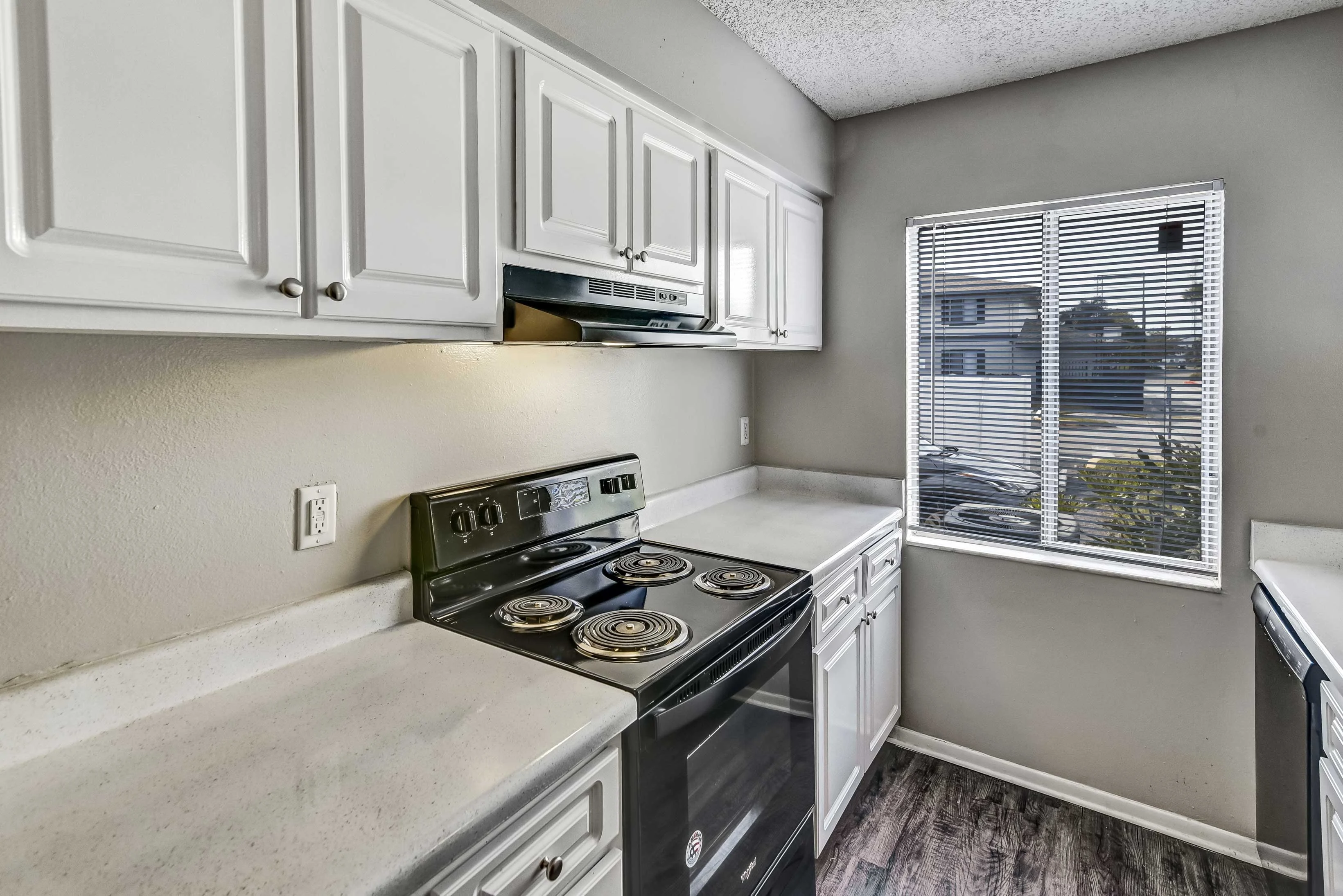 A modern kitchen with white cabinets, a black stove, and a window with blinds allowing natural light to enter.