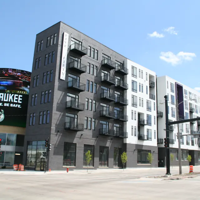 A modern multi-story building with balconies, located at an intersection, featuring a large digital billboard displaying a message about Milwaukee.