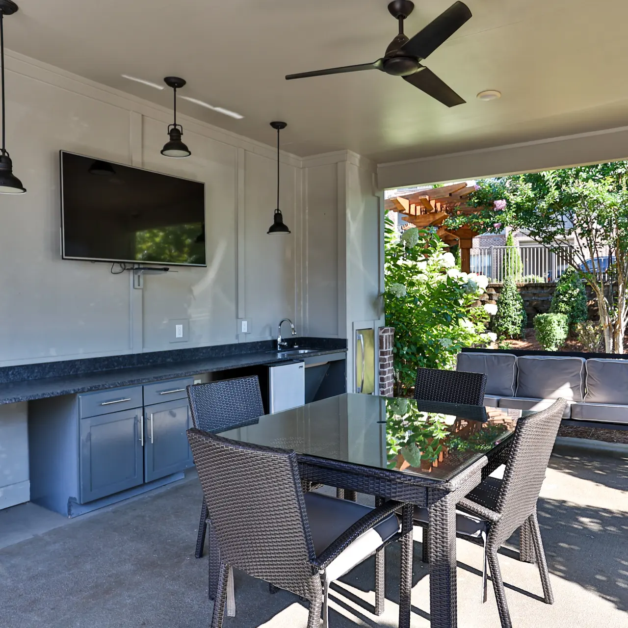 Stylish Outdoor Dining Area Covered outdoor dining area with a table and chairs, featuring a television and greenery in the background.