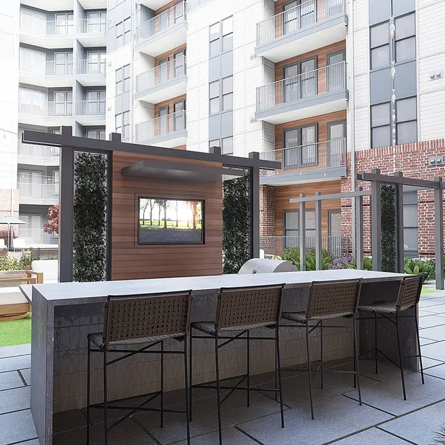 A modern courtyard area with a bar-style seating arrangement, surrounded by landscaped greenery and apartment buildings.