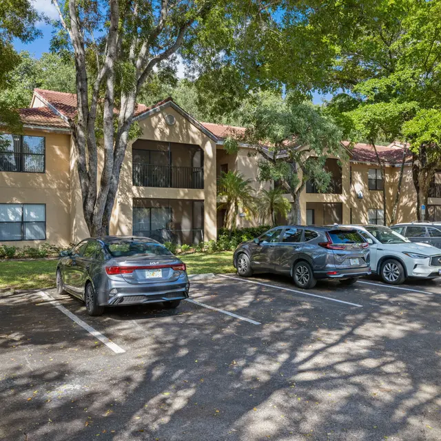 A view of a parking area in front of multi-story apartment buildings surrounded by trees.