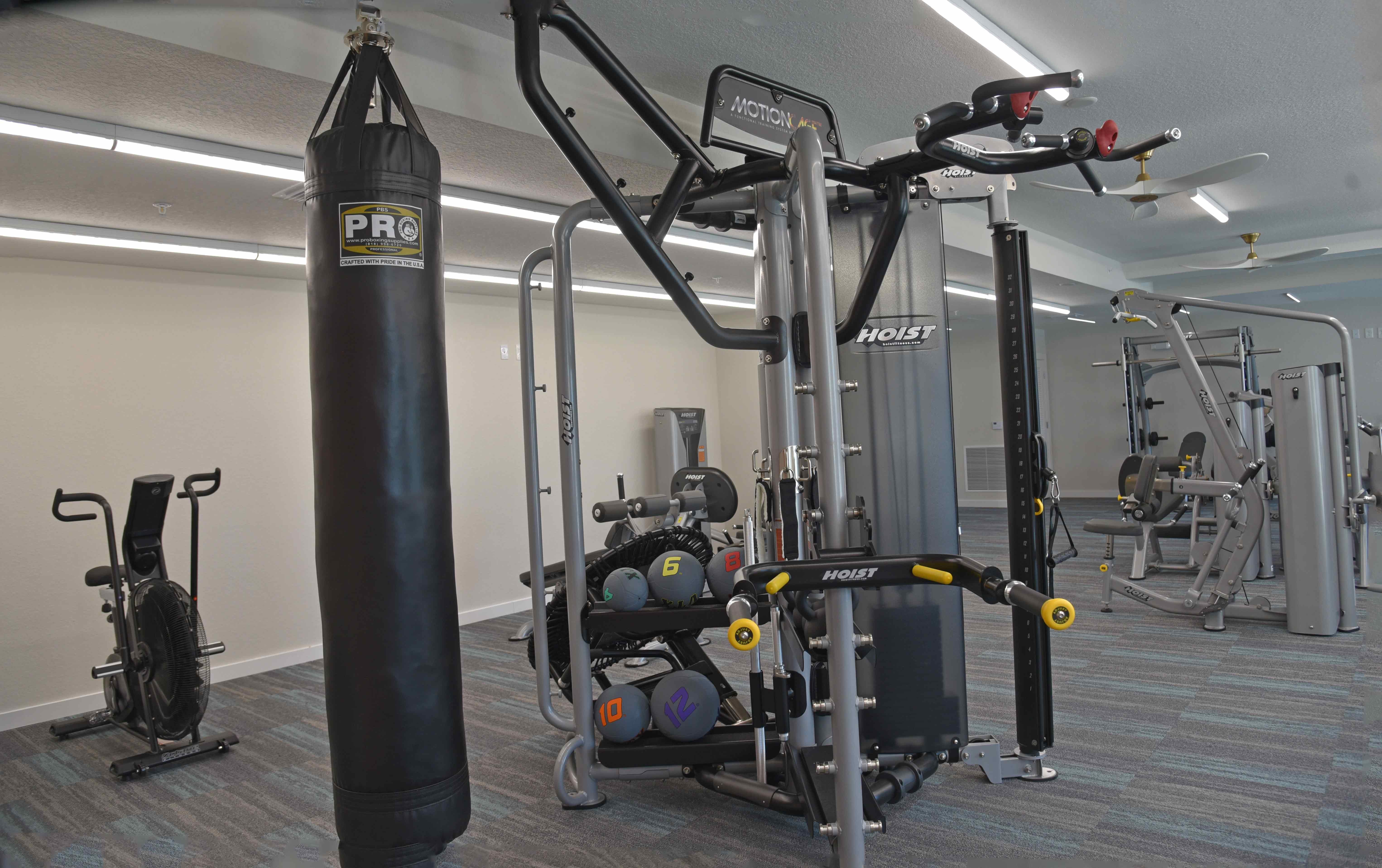 Interior of a gym featuring various workout equipment including a multi-station machine, a punching bag, and a stationary bike.