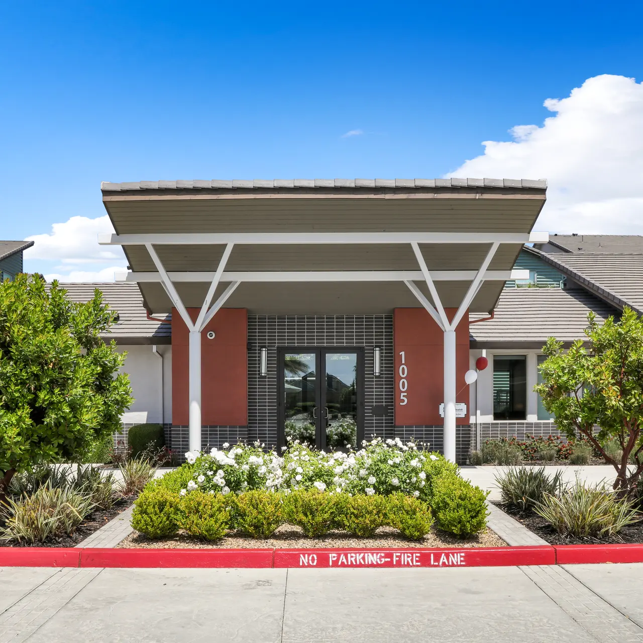 Modern apartment complex entrance with landscaping and a clear blue sky.