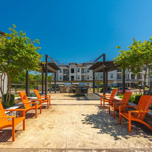 An outdoor gathering area with orange chairs surrounded by greenery and modern buildings in the background.