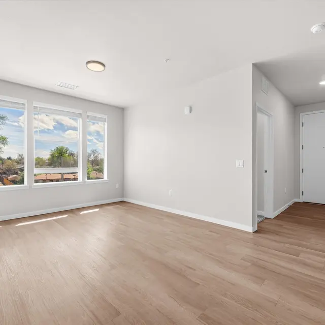An empty, bright room with large windows allowing natural light in and a wooden floor.