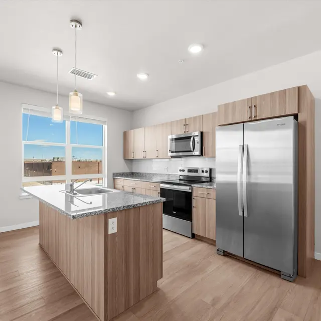 A modern kitchen featuring a central island, stainless steel appliances, and wooden cabinetry with large windows allowing natural light.