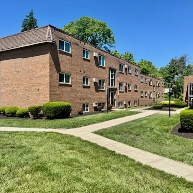 Apartment Complex on a Sunny Day A view of a brick apartment complex with multiple buildings, surrounded by well-maintained green lawns and pathways.