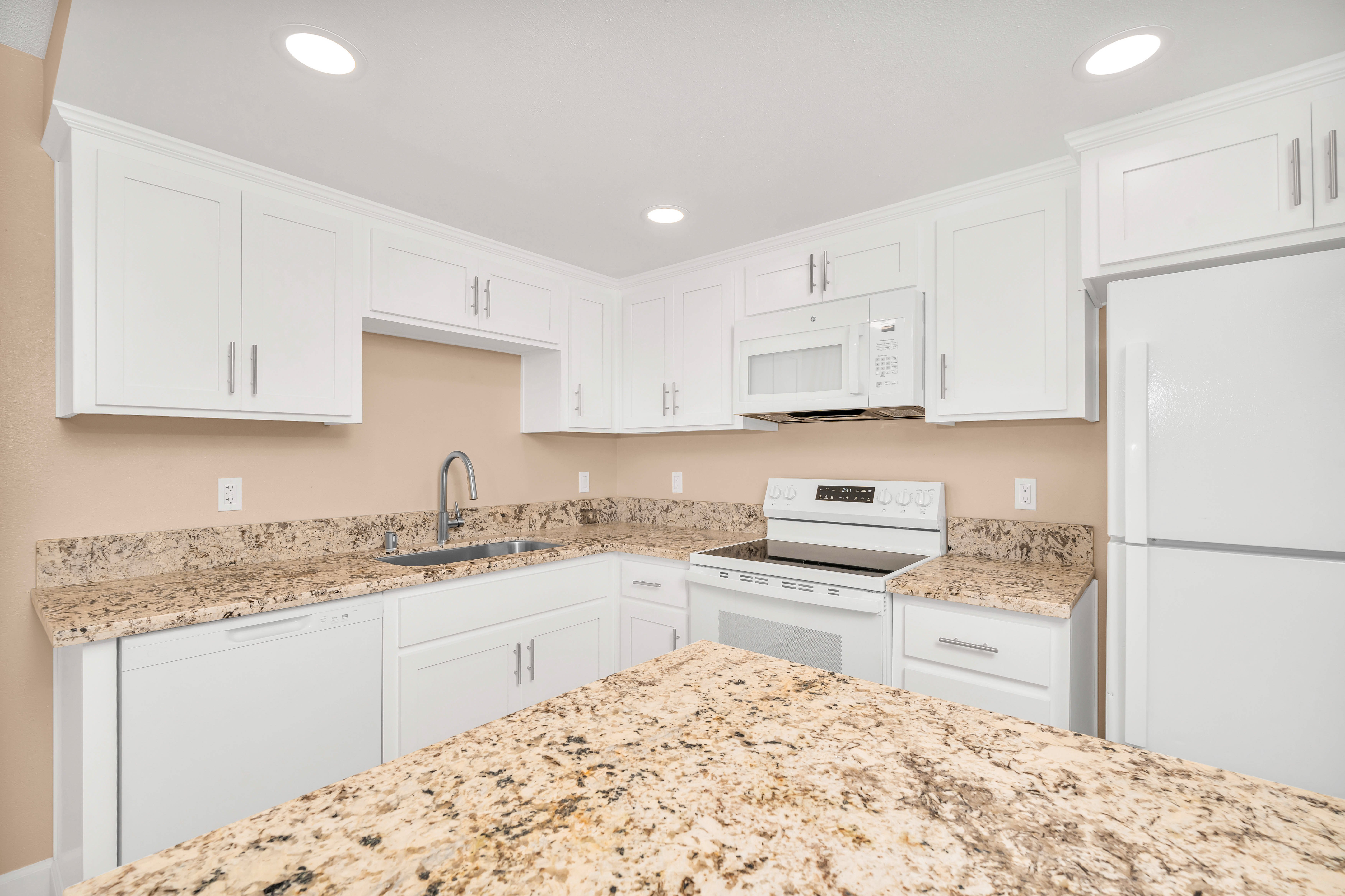 A modern kitchen featuring white cabinetry and granite countertops. Equipped with stainless steel appliances including a stove, refrigerator, and microwave.