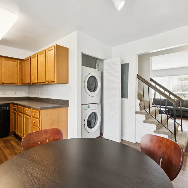 Modern Kitchen and Living Room A bright and spacious kitchen area with wooden cabinets and a round dining table, adjacent to a living room with a staircase leading up.