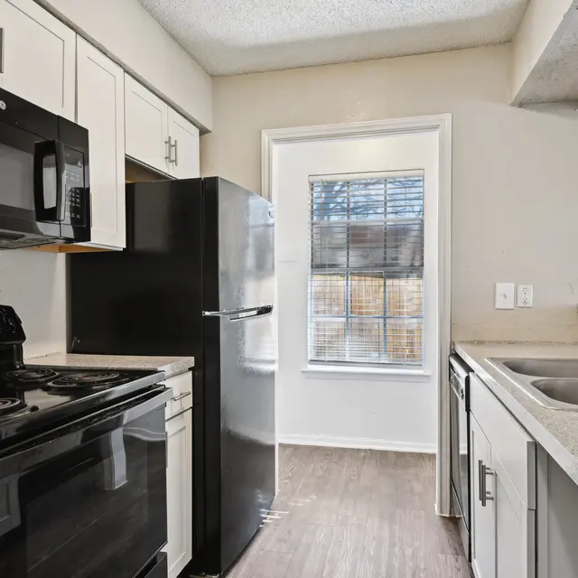 Modern kitchen featuring a black stove, microwave, and refrigerator, along with light-colored cabinets and a window.