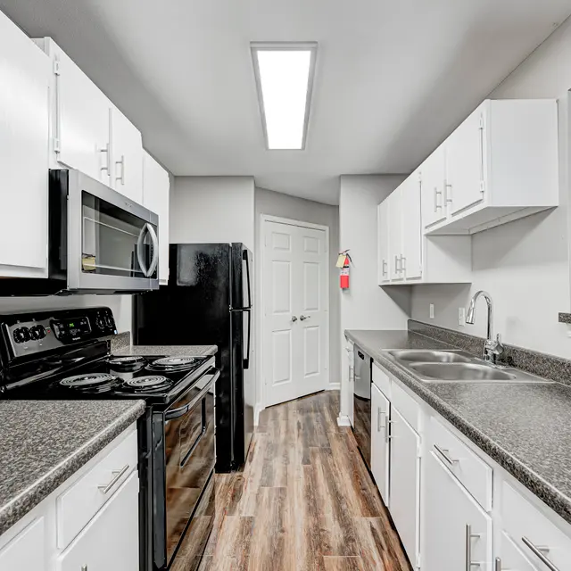 A modern kitchen featuring white cabinets, dark countertops, stainless steel appliances, and wooden flooring.